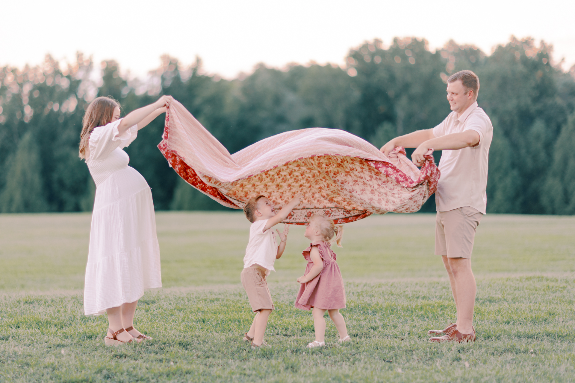Parents holding quilt while kids play London Bridges in Dallas GA maternity session