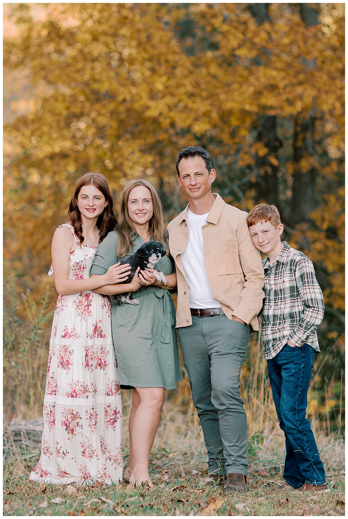 Family of four with their small black and white dog during a fall portrait session beneath colorful autumn trees at White Oak Park in Dallas, Georgia.