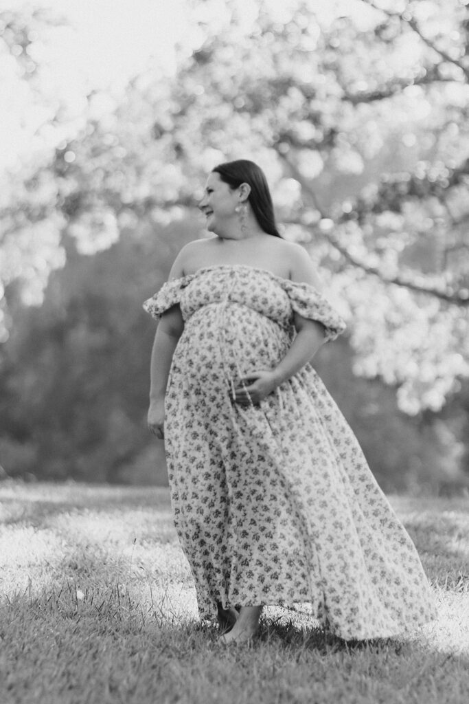 Black-and-white maternity portrait of Abby holding her belly beneath the trees at White Oak Park.