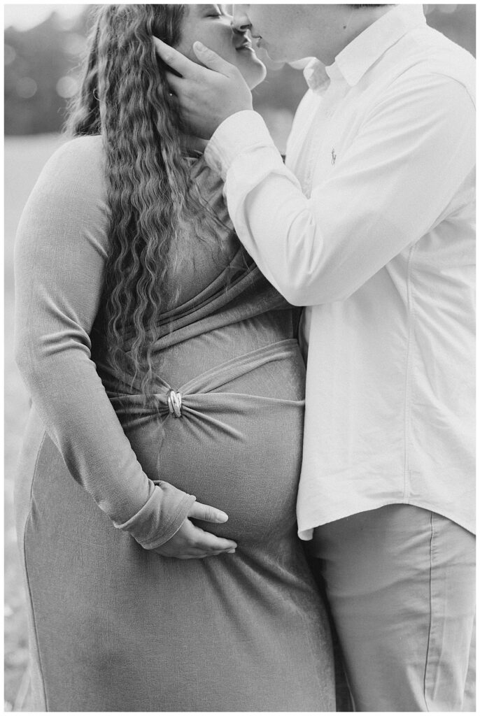 Close maternity portrait of expecting parents holding hands and resting hands on baby bump.