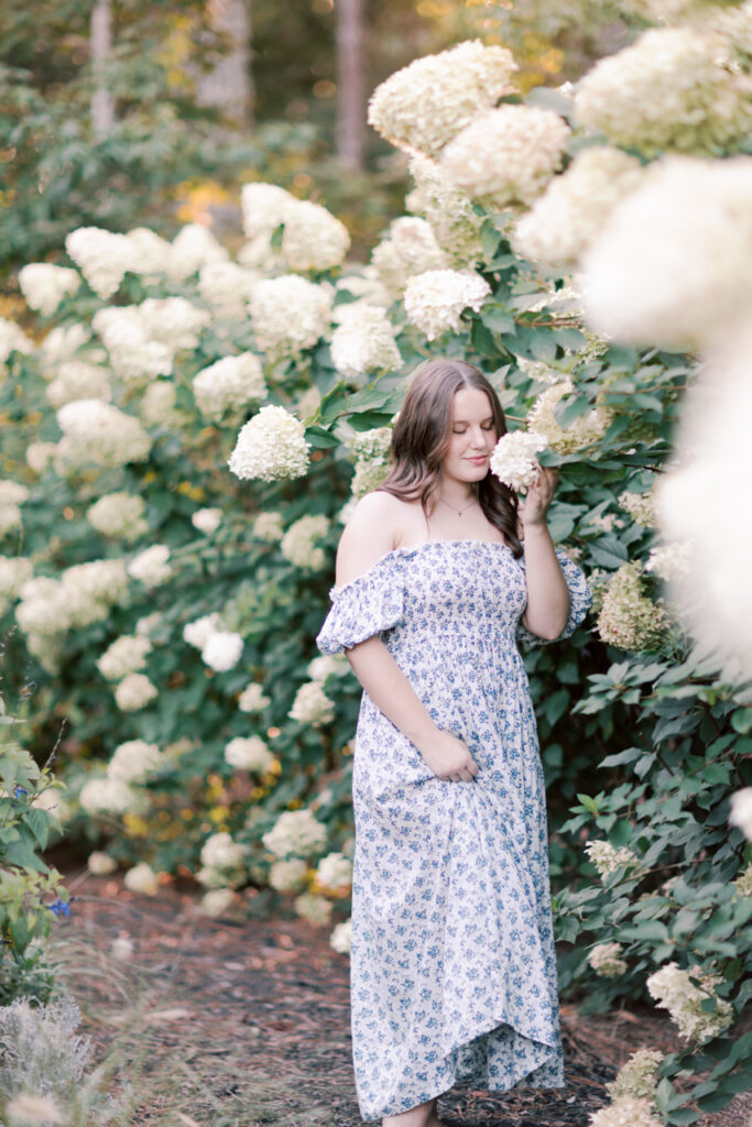 Young woman in a blue floral dress standing among white Limelight hydrangeas.