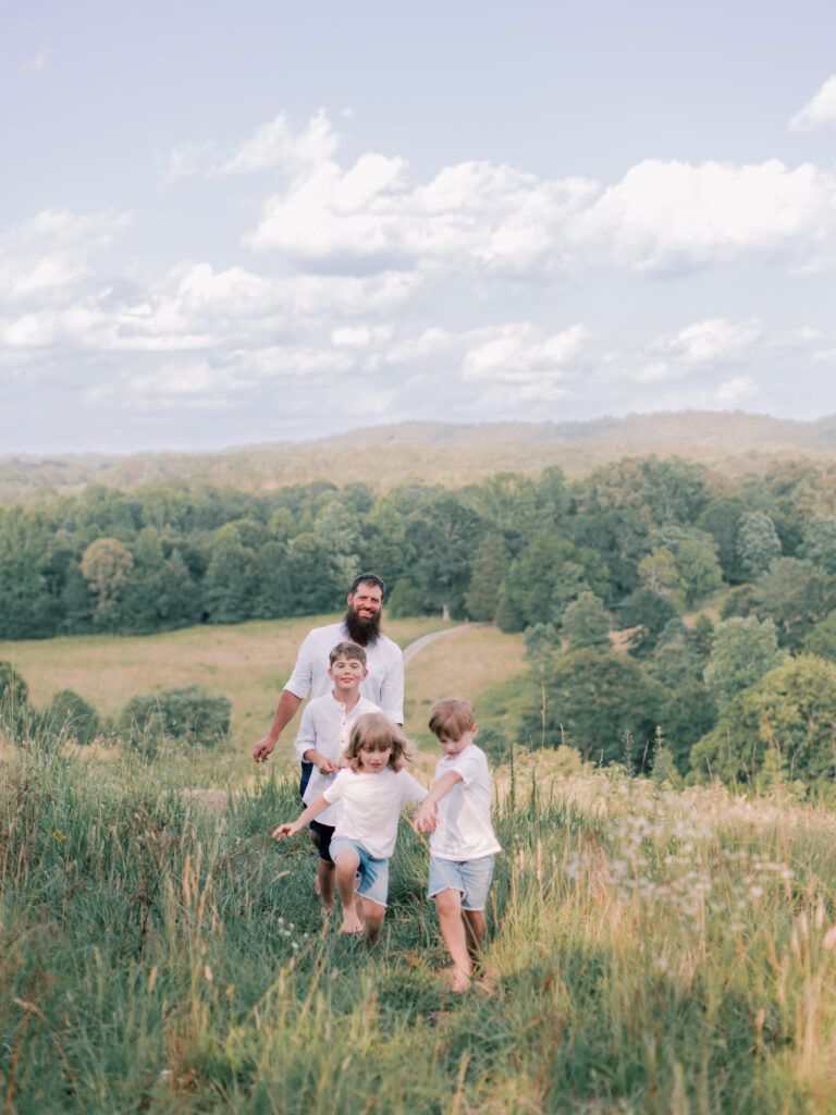 Father running outdoors with his three young children during a family session.