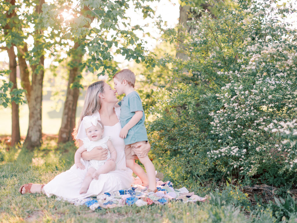 Mother holding her baby daughter while her young son leans toward her outdoors.