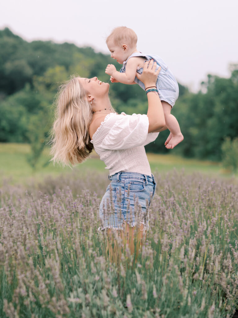 Mother smiling up at her baby while lifting him above a wildflower field.
